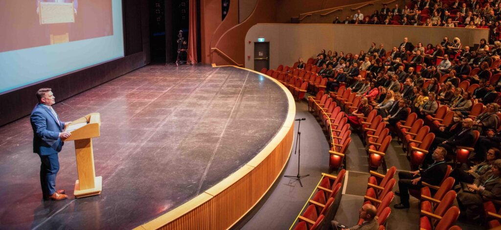 Photo of theater stage with crowd listening